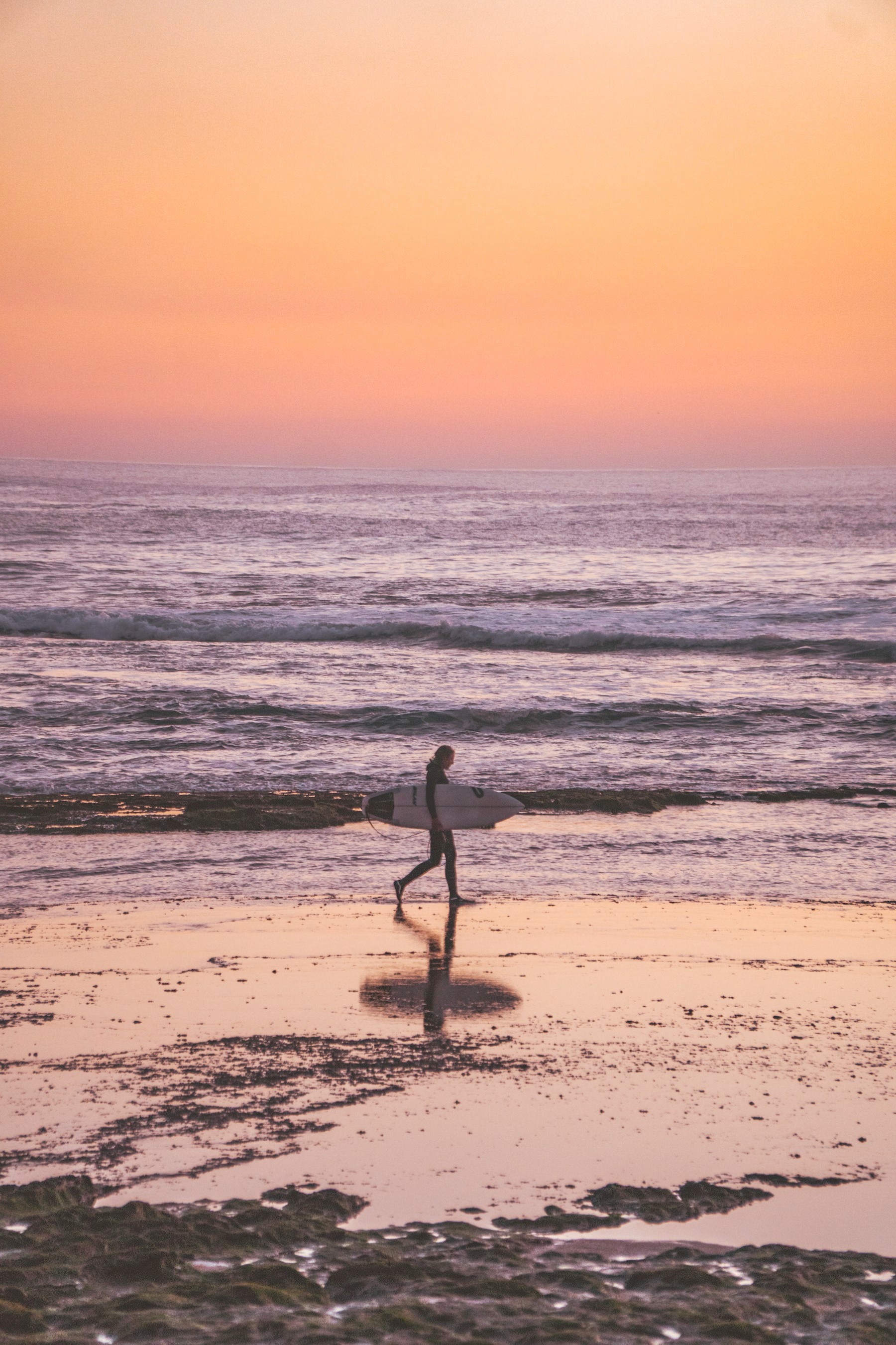 Surfer walking with a board at sunset after a full surf day